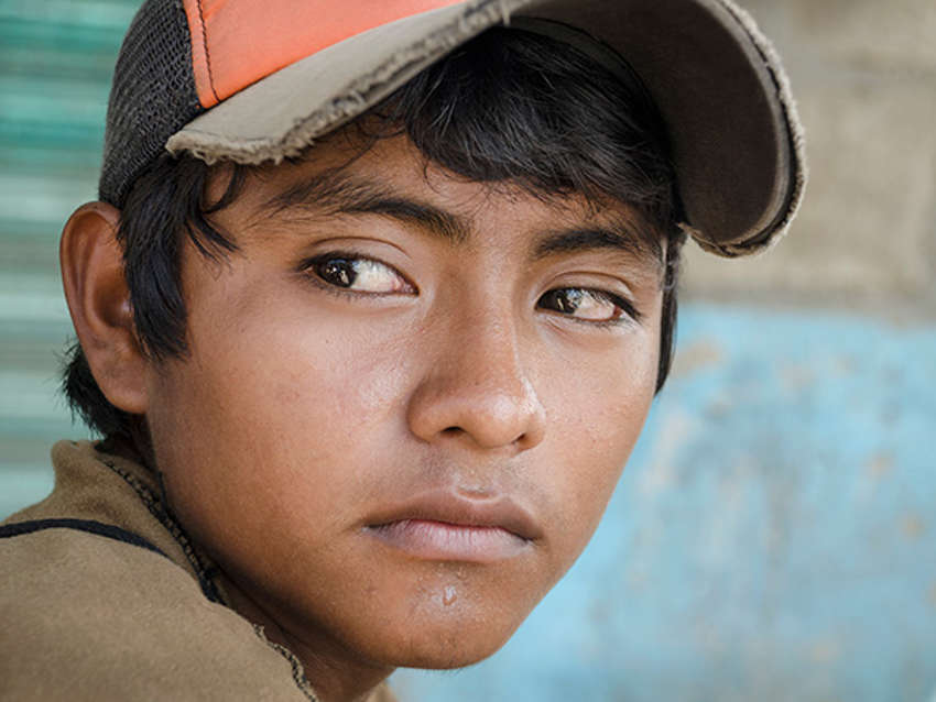 A profile view of a  refugee mom carrying her young children past a graffitied wall.