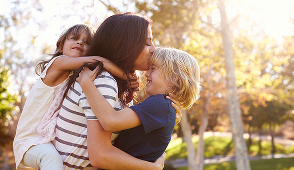 mother hugs her two young children at sunset