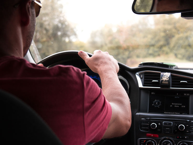 white man holds the wheel of his car while driving