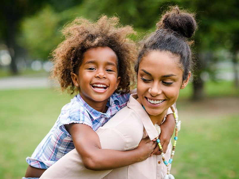 african american birth mother holds her daughter on her back during an open adoption visit