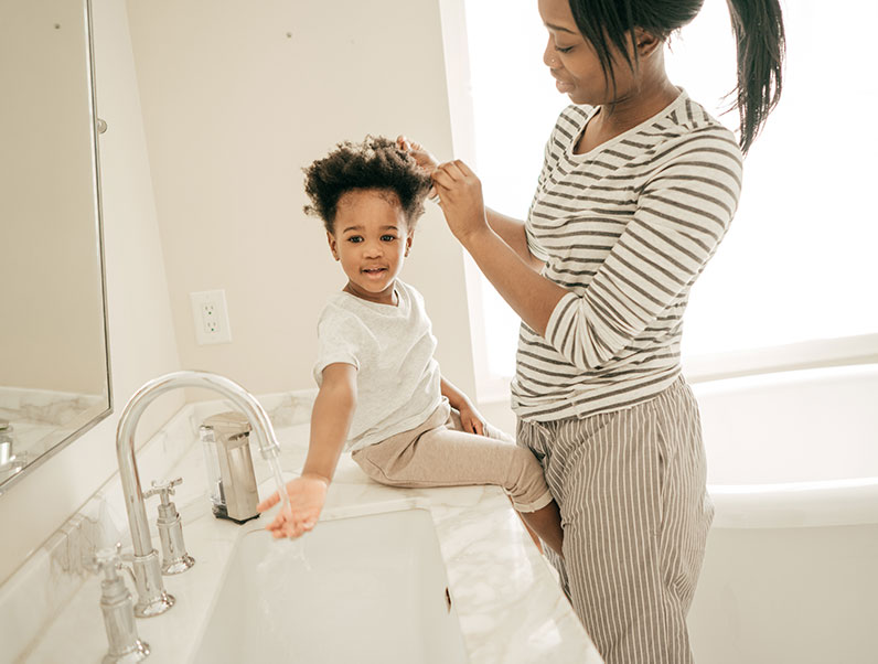 african american mother does her daughter's hair in the bathroom